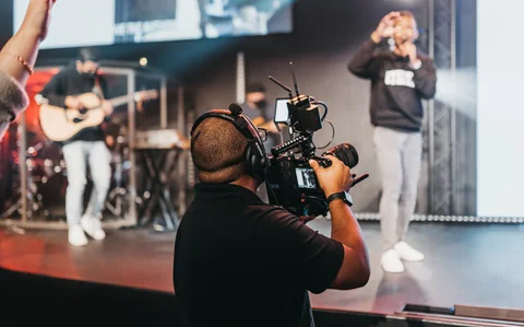 A camera operator wearing headphones records a speaker onstage during a Radiant Church service.